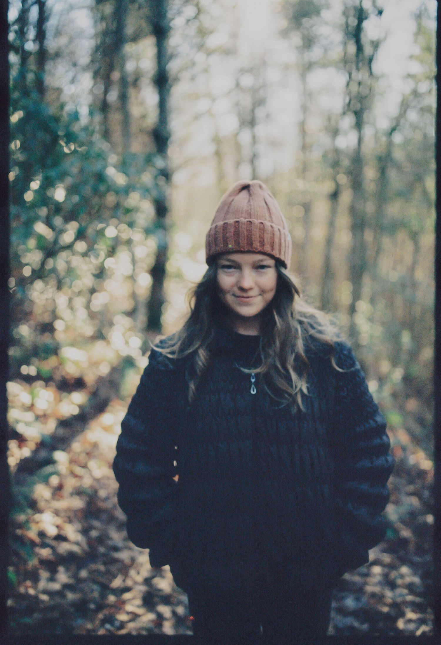 Forest scene with someone wearing a brown knit beanie and dark coat among autumn trees.