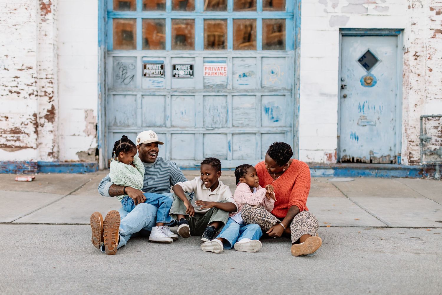 People sit and relax outside a weathered building with bright blue doors and windows in a casual street scene.