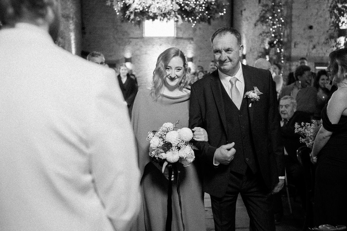 A black and white wedding ceremony processional shows a couple walking down the aisle together with a bridal bouquet.