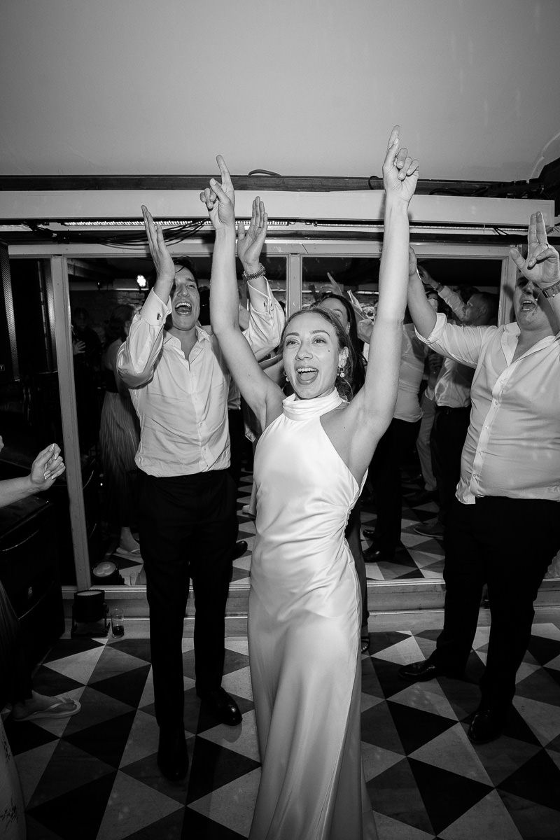 A sequence of black and white photos showing people dancing with raised arms on a checkered floor at a celebration.
