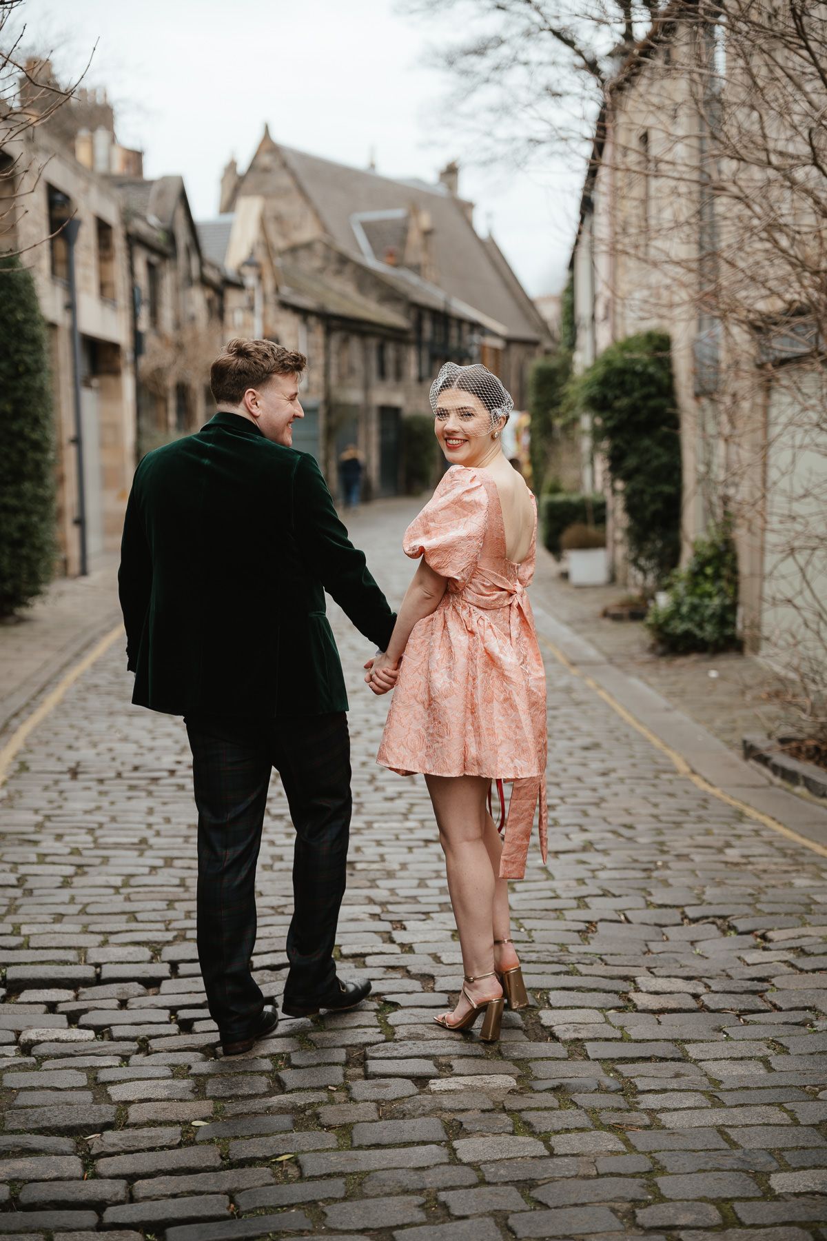 A couple strolls down a charming cobblestone street lined with historic stone buildings.