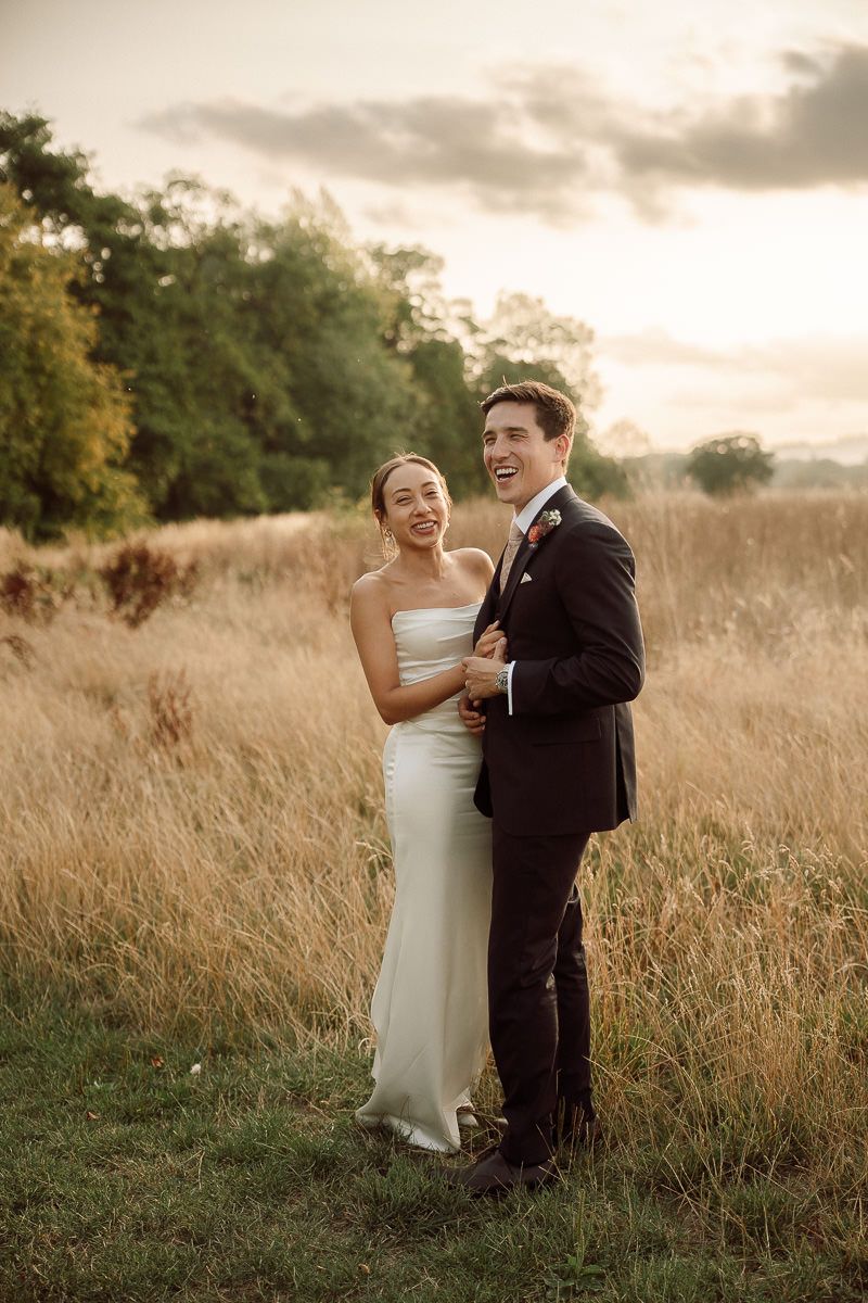 A couple shares a romantic moment in a golden field at sunset, dressed in formal wedding attire.
