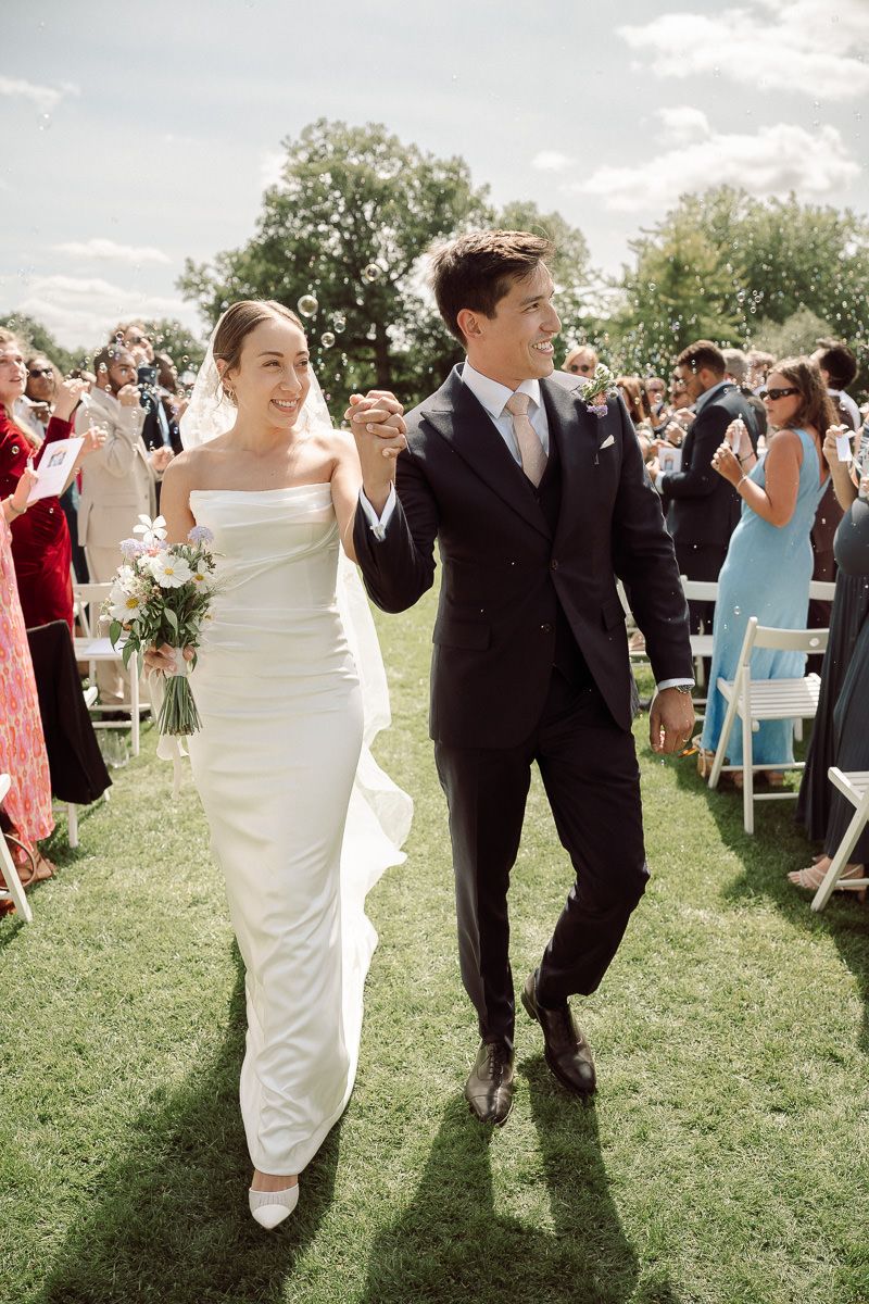 Wedding guests celebrate on a sunny outdoor lawn with people in formal attire dancing and mingling.