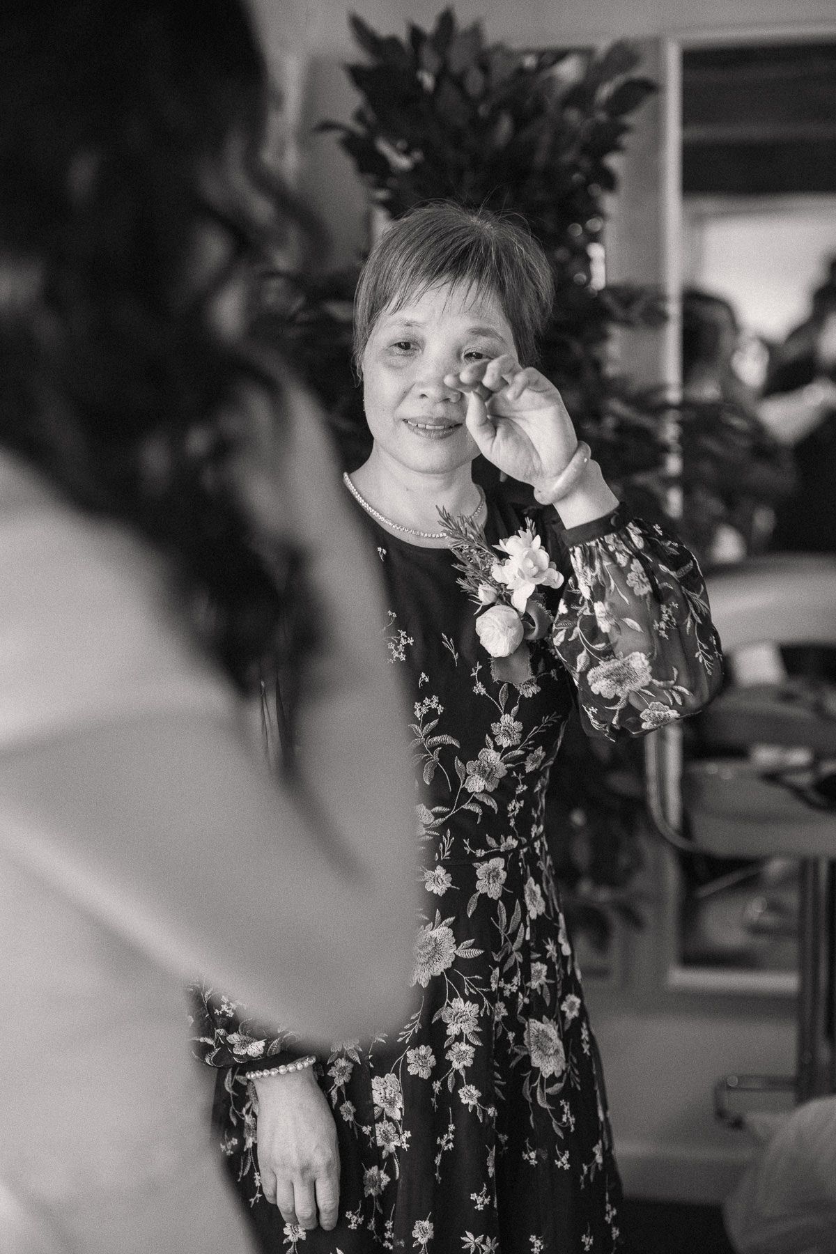A black and white photograph of a smiling woman wearing a floral dress and looking at the camera.
