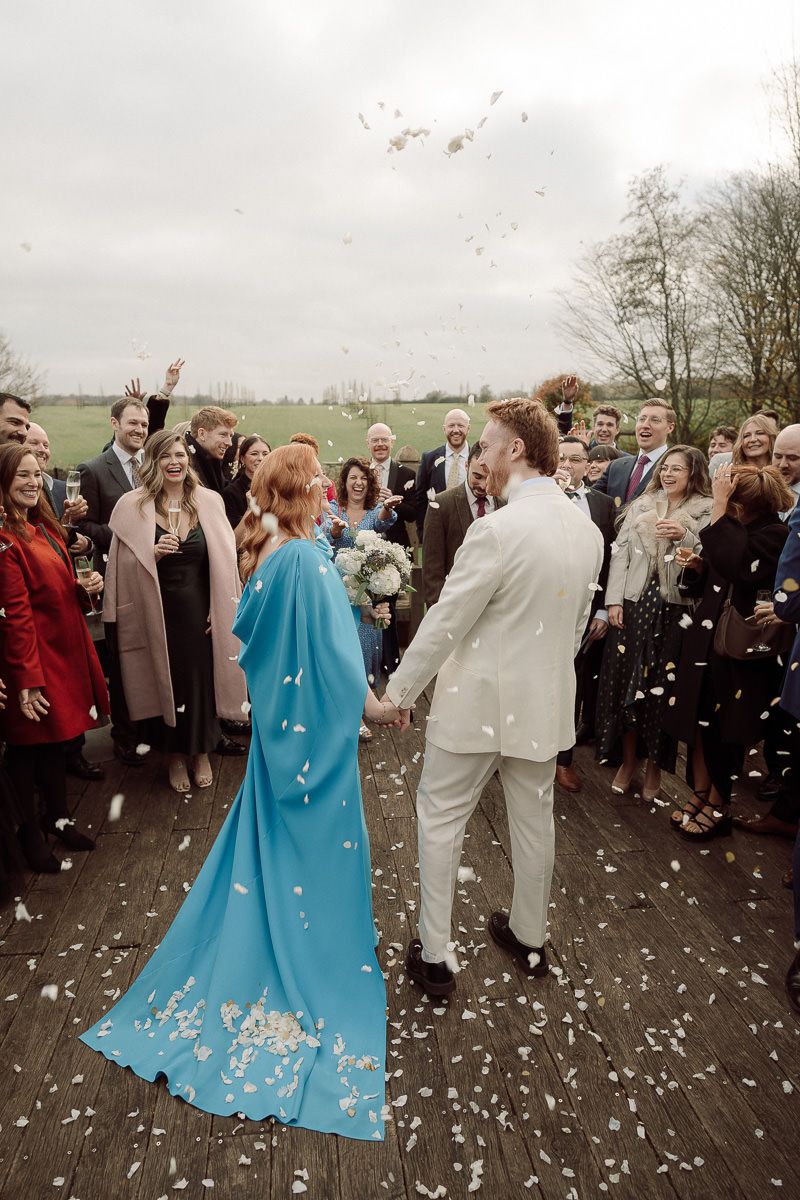 Wedding guests celebrate with confetti as newlyweds in light and turquoise attire share joyful moments outdoors.