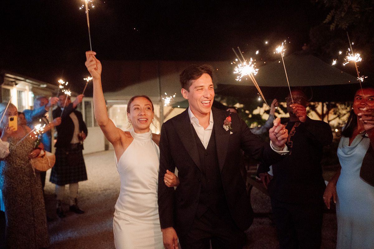 Wedding guests hold sparklers creating a magical nighttime celebration atmosphere outdoors.