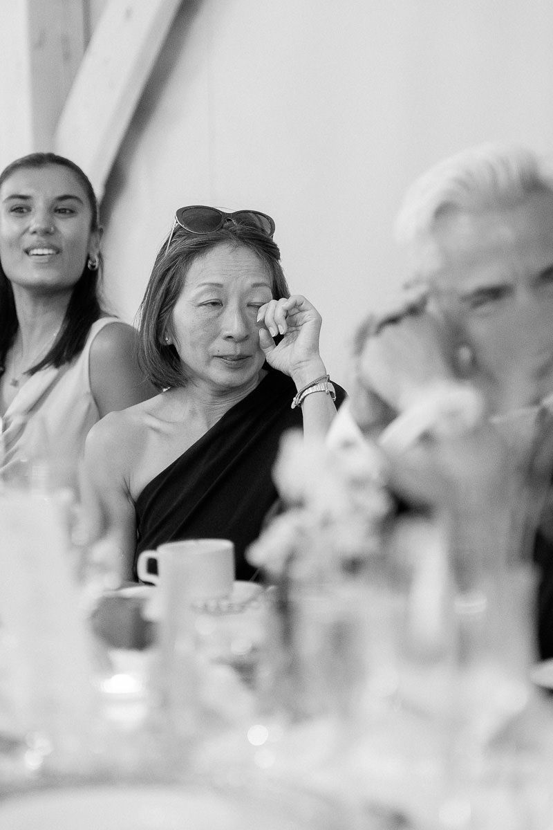 Black and white candid photograph of guests at a formal event with cups and table settings visible.
