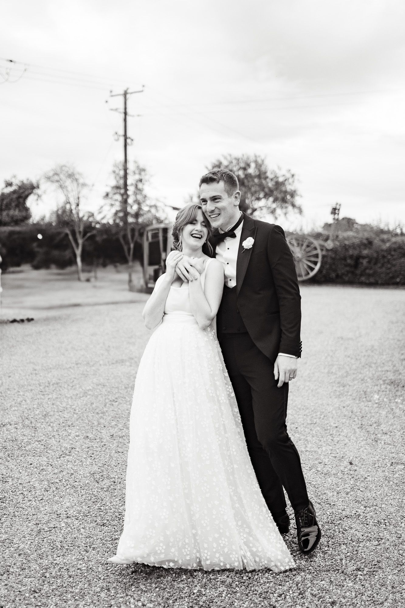 A couple in formal wedding attire embracing while standing together in a grassy outdoor setting.