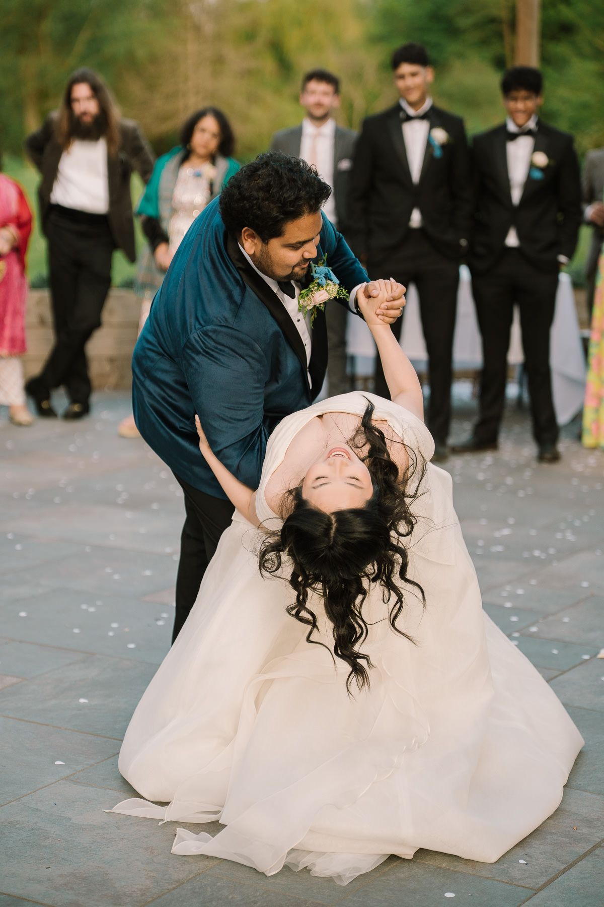 A wedding couple embracing on a dance floor with their wedding party in the background.