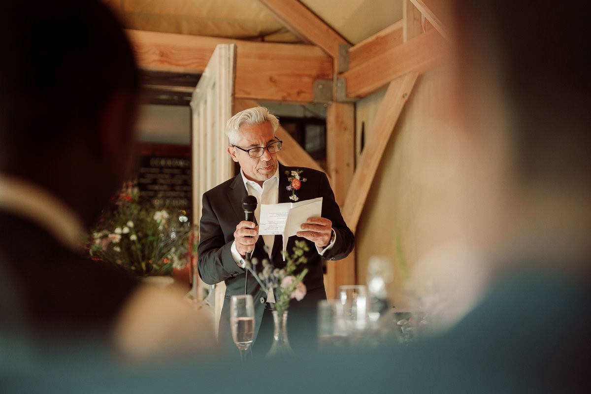 Wedding guests share laughter and conversation at a rustic wooden venue with warm lighting.