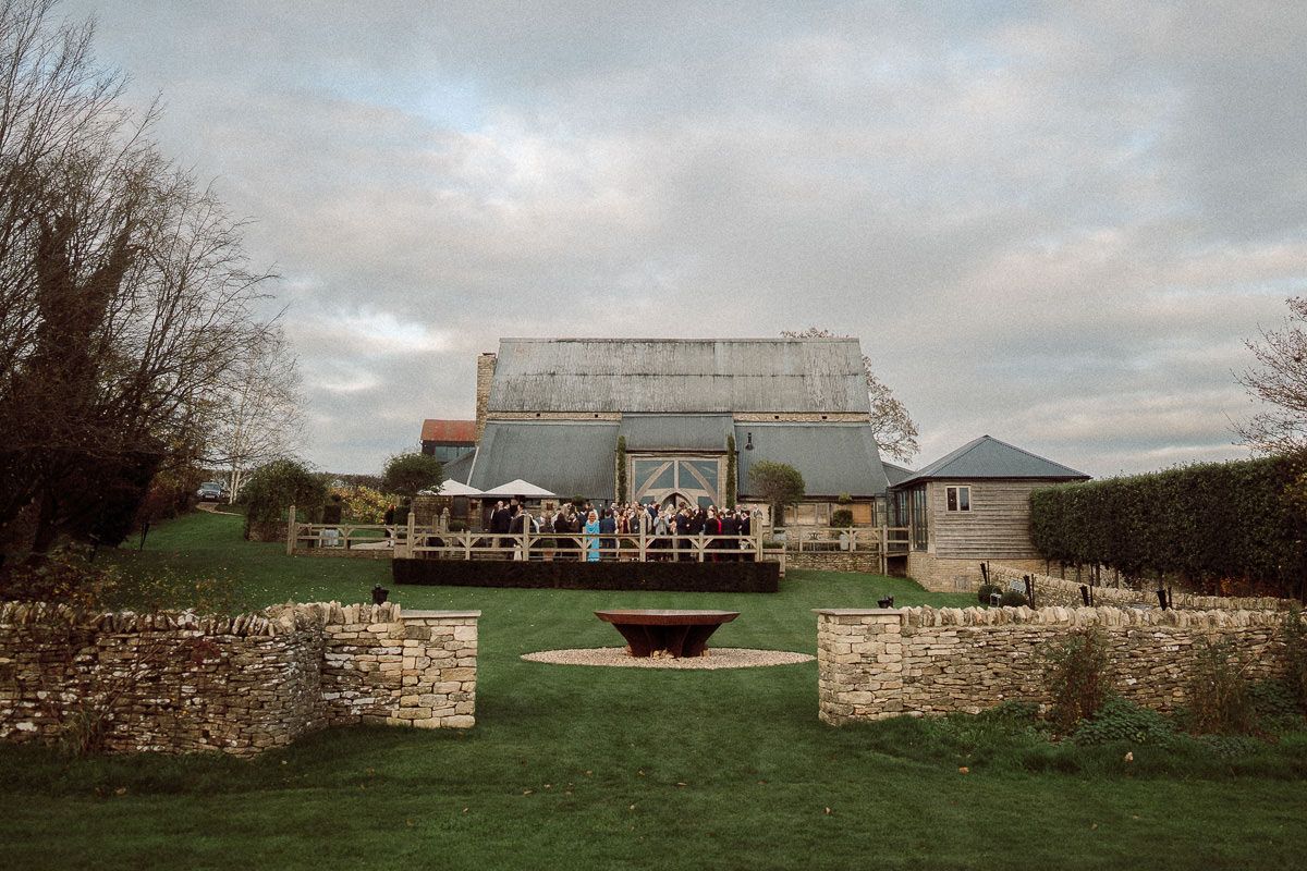 A panoramic view of a rustic stone building and grounds with cloudy skies overhead.