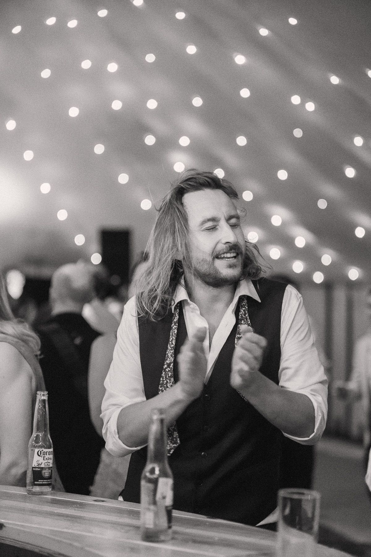 A man with long hair and a beard smiling and laughing at a bar or restaurant.