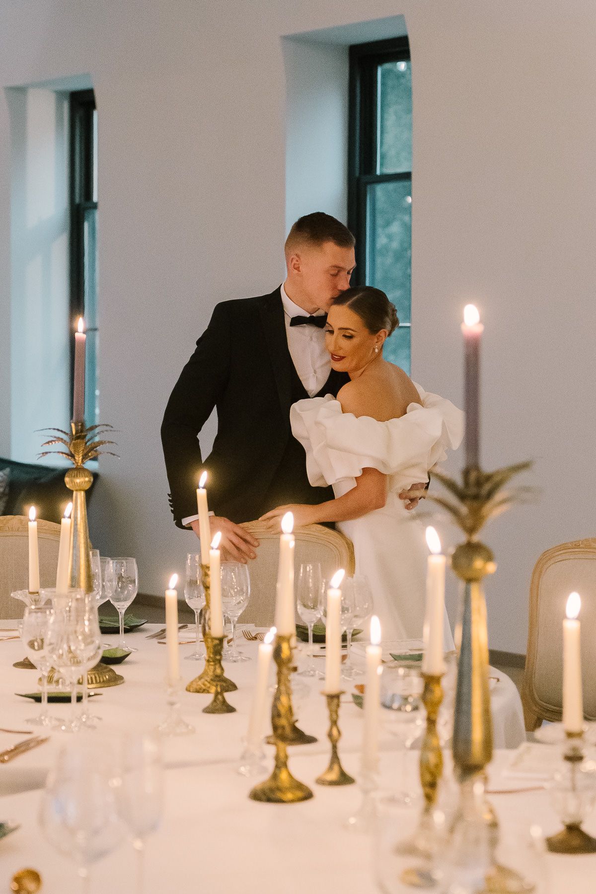 A bride and groom standing at a candlelit table, embracing each other in a romantic wedding scene.