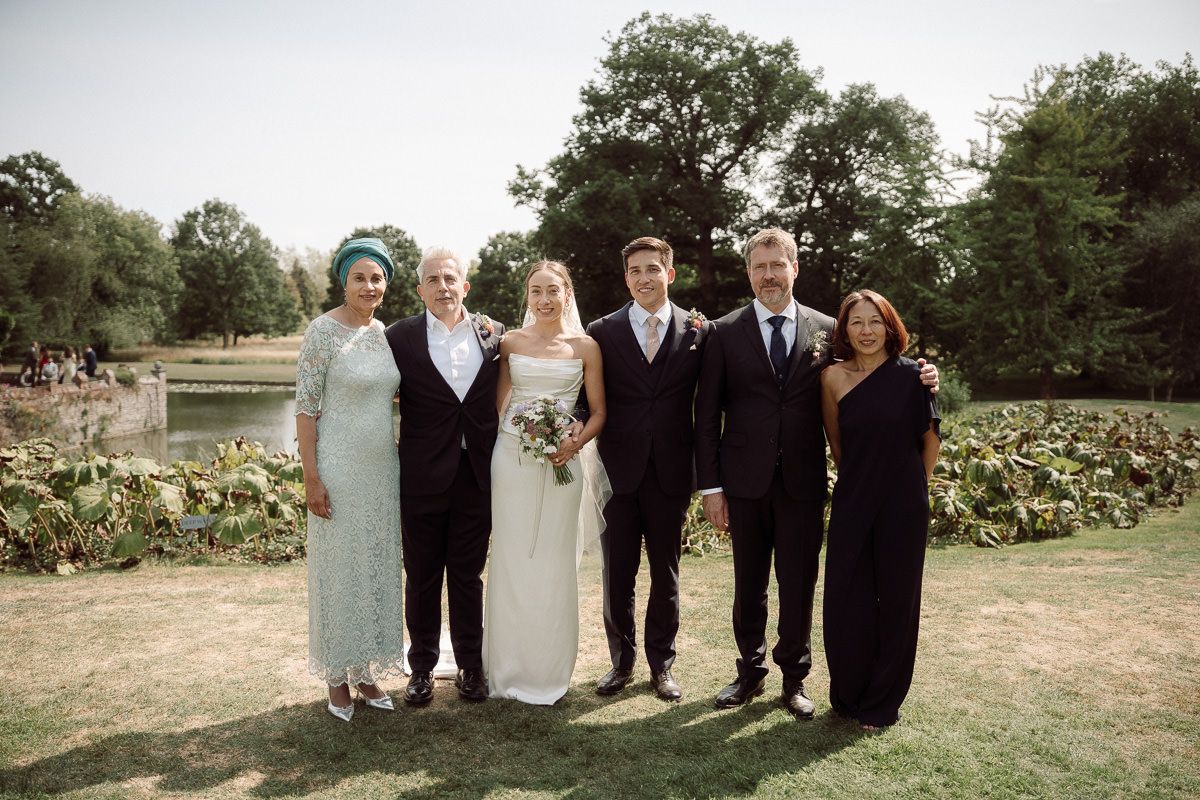 Wedding party poses together in a garden setting with greenery and natural outdoor scenery in the background.