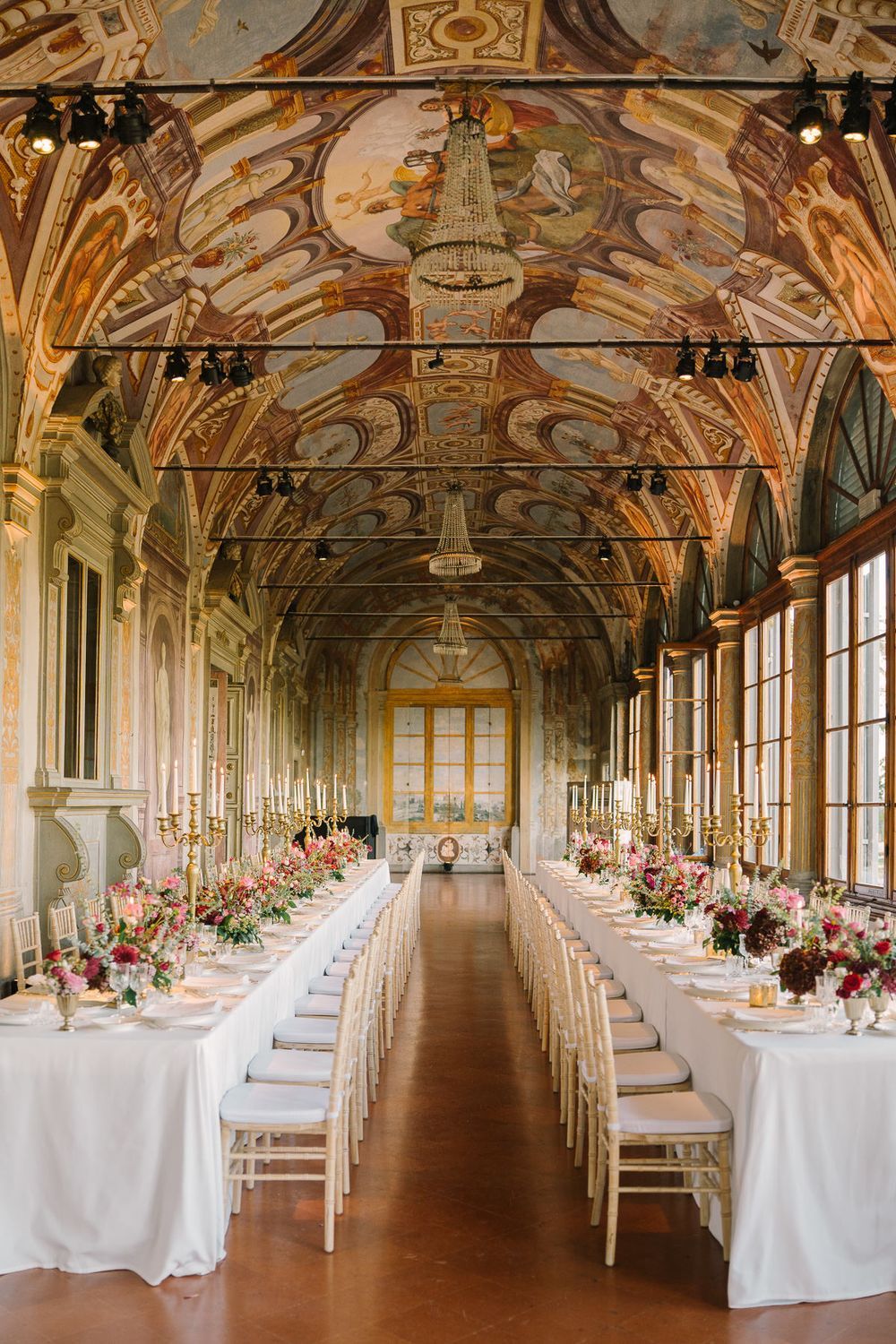 Elegant wedding reception in a historic Italian villa with frescoed ceilings, long white tables, and floral centerpieces.