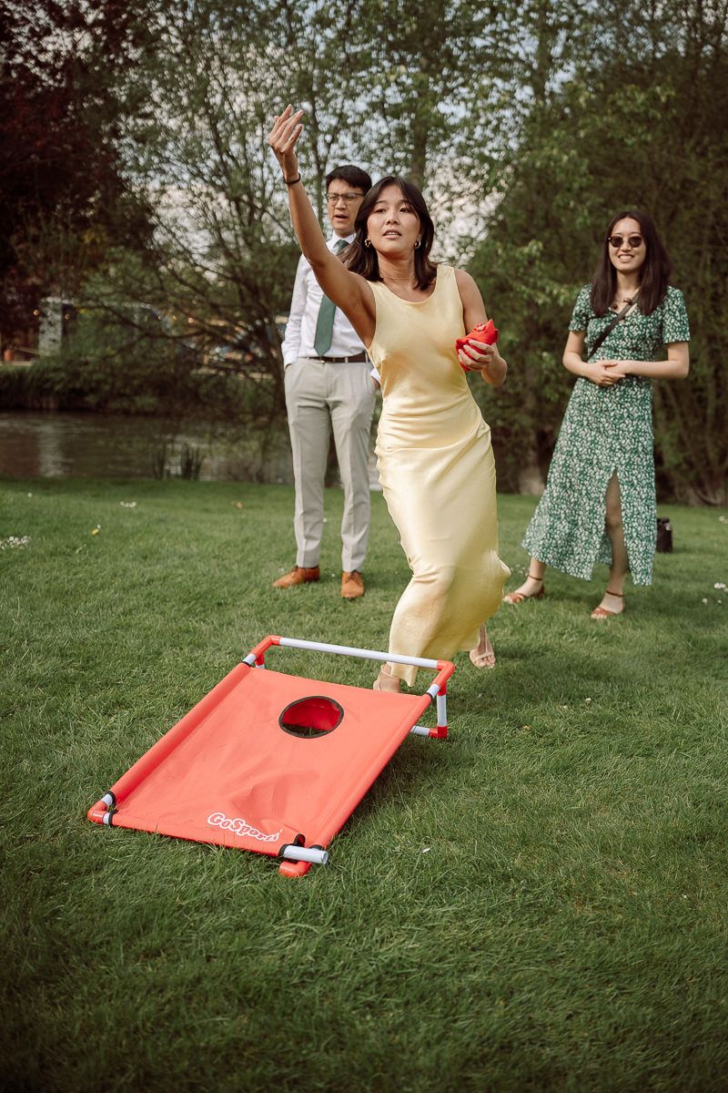 A group of people playing cornhole on a grassy lawn at an outdoor gathering.