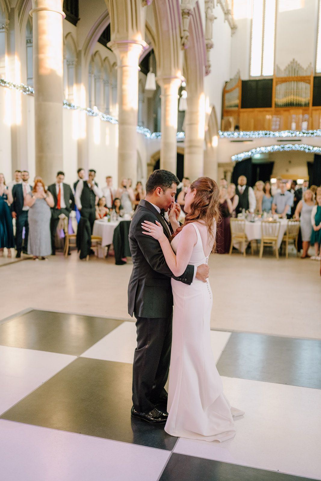 Bride and groom share their first dance on a checkered floor inside an elegant church wedding venue.