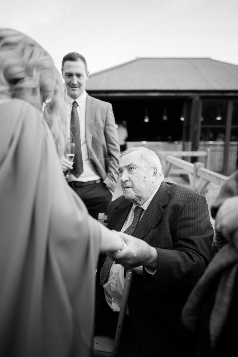 A black and white candid shot of guests mingling at an outdoor social gathering.