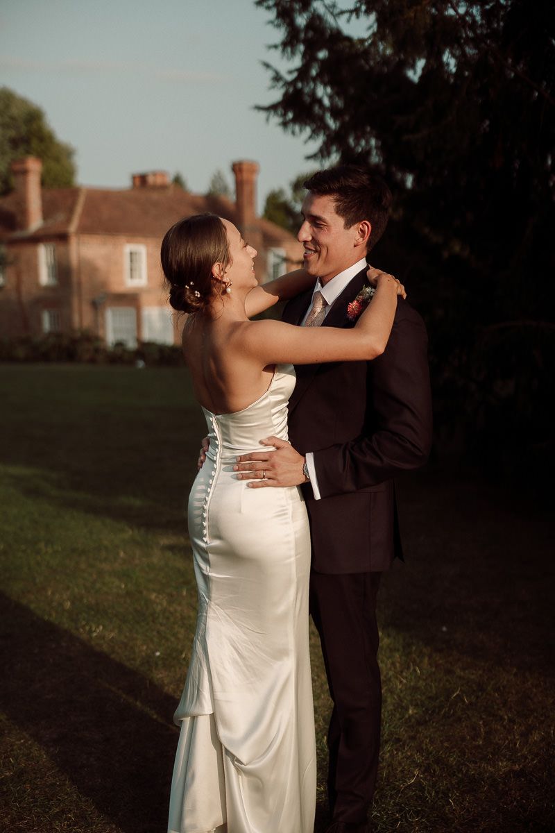 A bride and groom share an intimate moment outdoors at dusk with a historic building in the background.