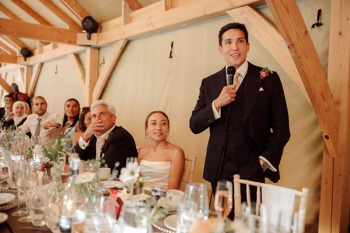 Wedding reception guests enjoying a celebration dinner in a rustic barn venue with exposed wooden beams and elegant table settings.