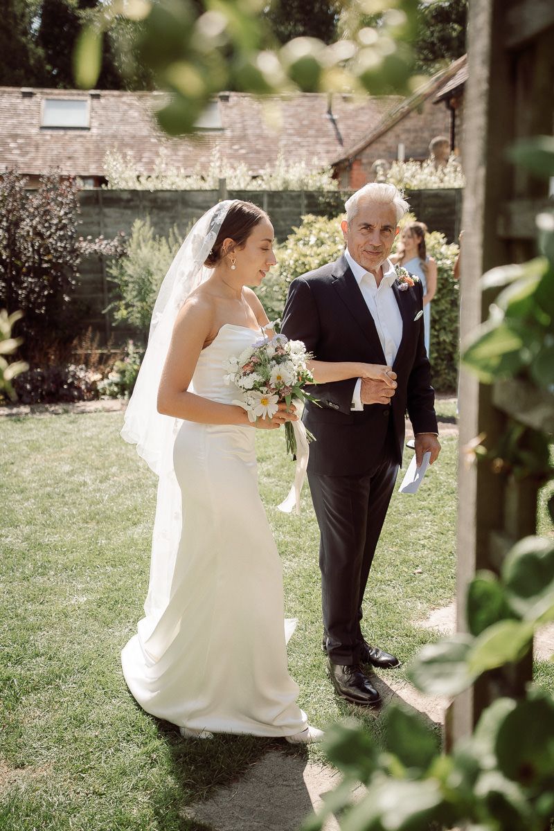 Newlyweds walk together on a grassy path beside stone walls during their wedding celebration.