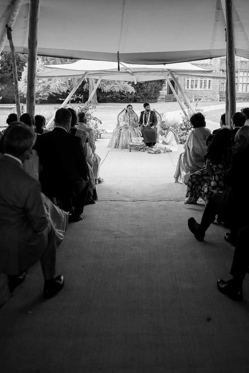 Black and white photo of an outdoor wedding ceremony under a tent canopy with guests seated in rows.