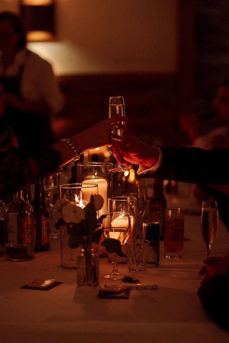 A dimly lit table with wine glasses and bottles creating a moody, romantic restaurant atmosphere in warm lighting.