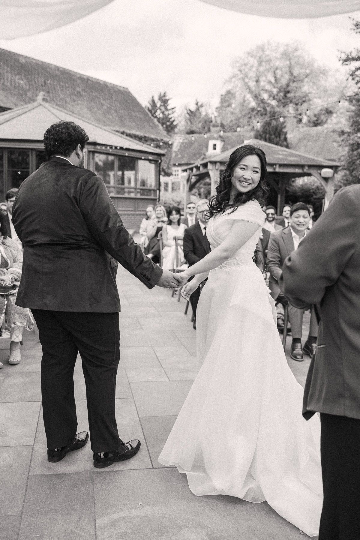 A bride in a white dress and veil is walking with her groom in a formal suit at an outdoor wedding ceremony.