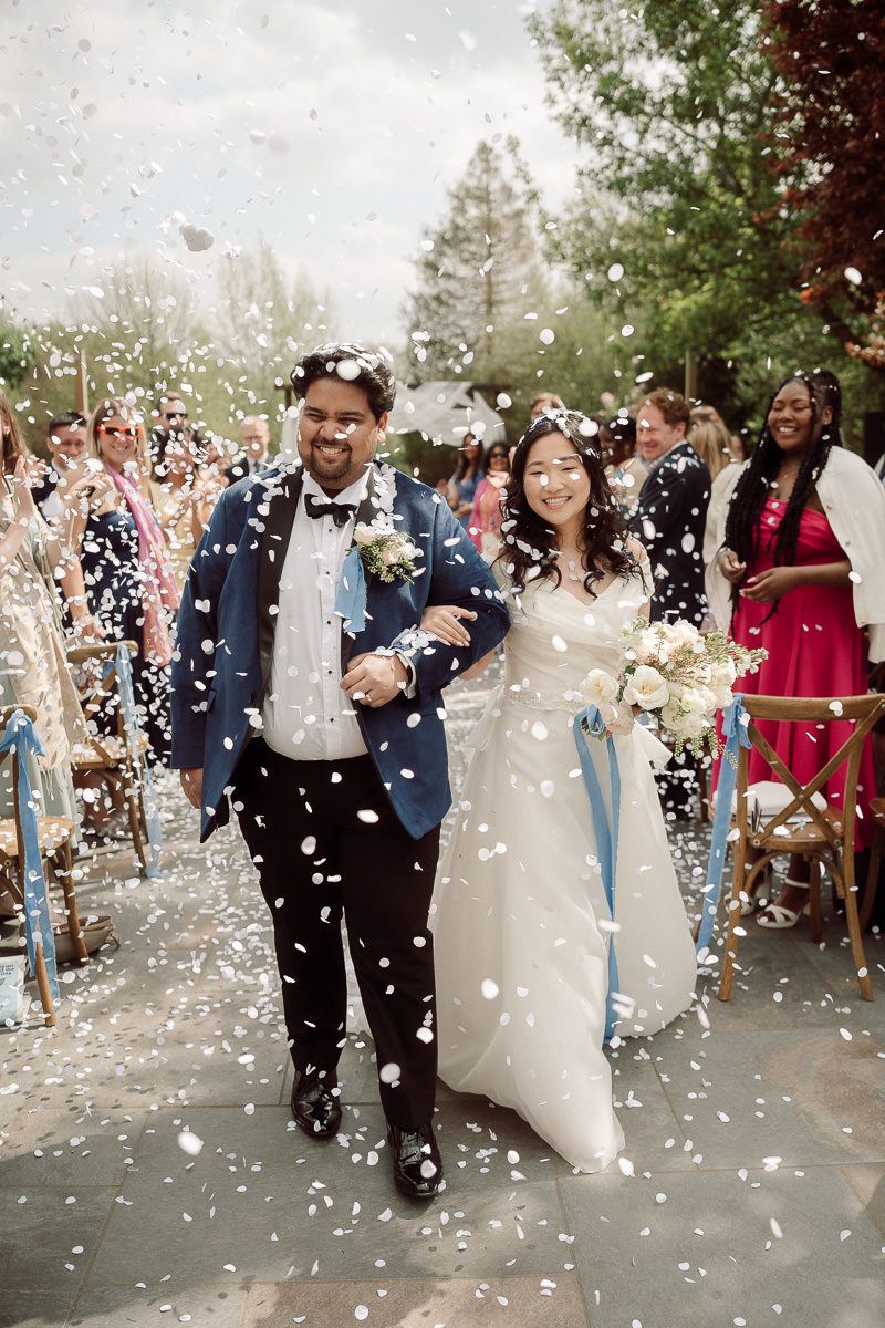 Wedding guests shower newlyweds with white confetti petals during outdoor celebration.