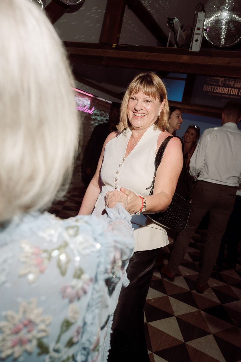 A joyful guest laughs while sitting at a wedding reception table with decorative white floral centerpieces.