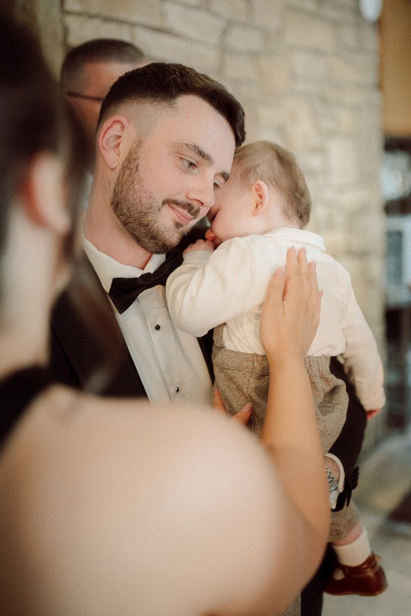 Two people share an intimate moment in formal attire at a wedding reception with stone walls in the background.