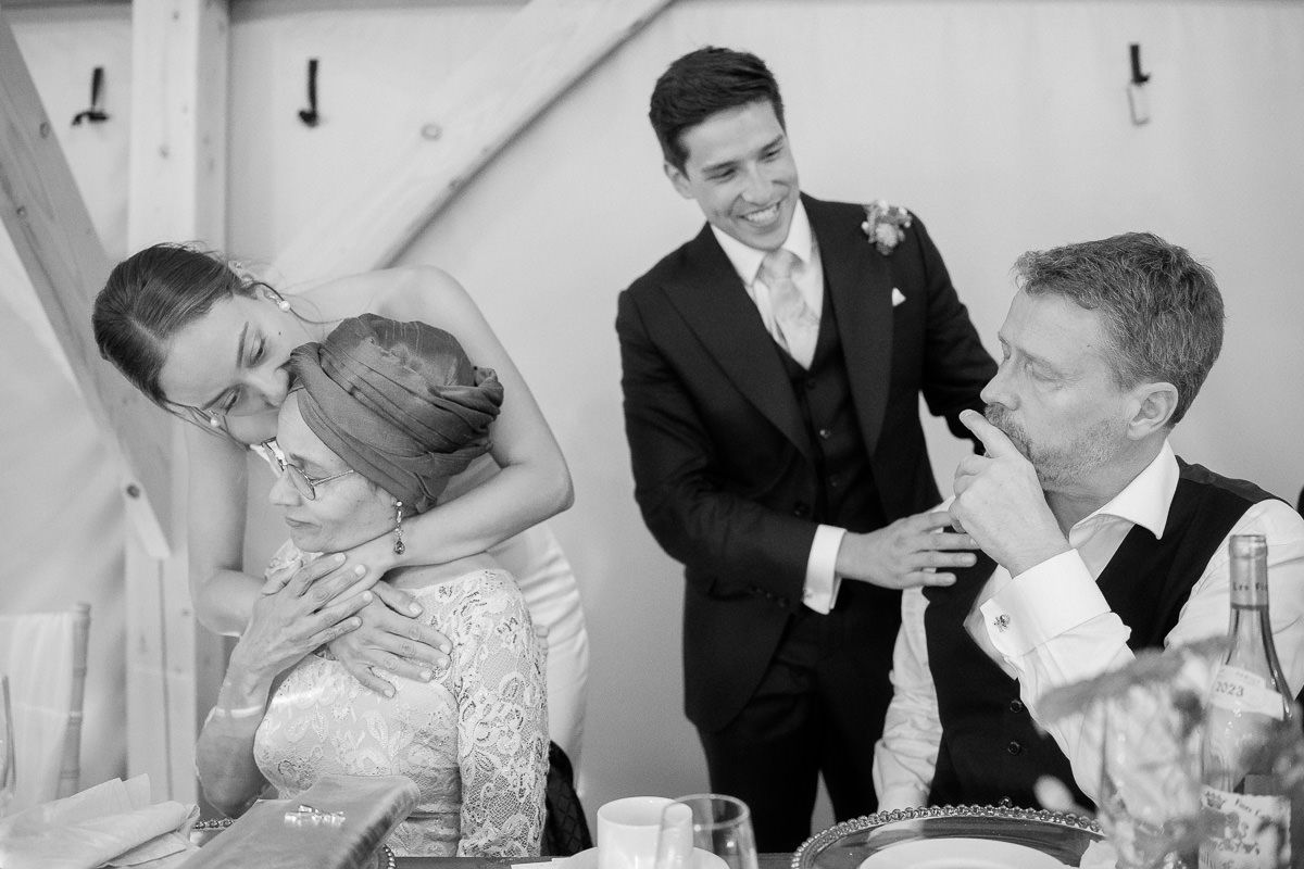 Black and white wedding reception photo showing emotional moments between guests at a dining table.