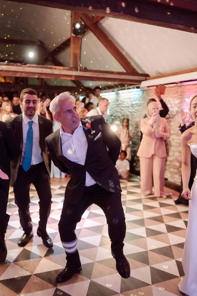 Wedding guests perform synchronized dance moves on a black and white checkered dance floor at a reception.