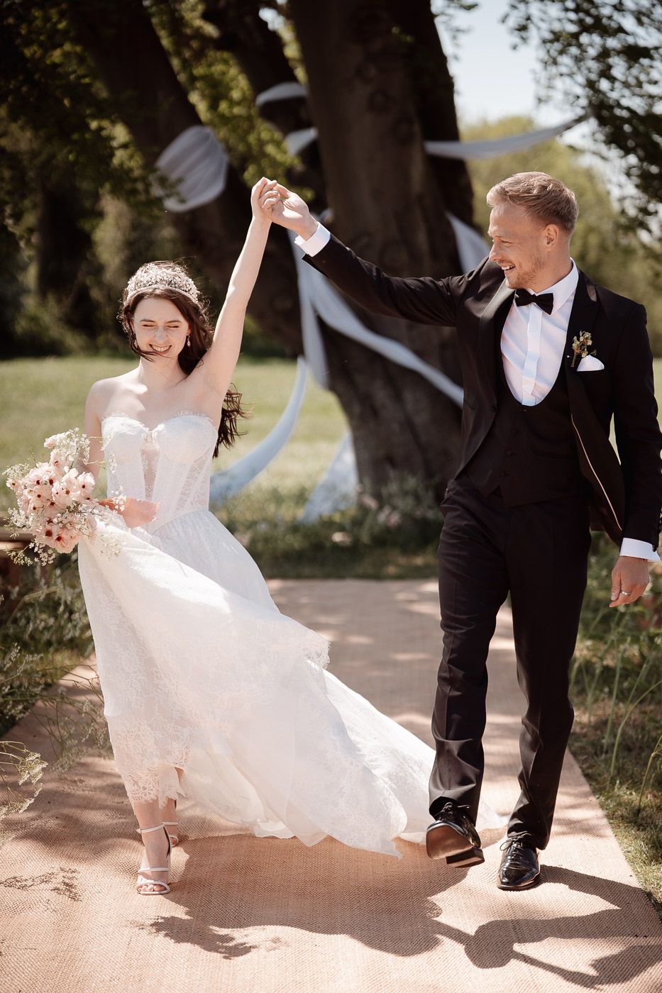 Five sequential photos show a couple dancing and twirling together outdoors in wedding attire on a sunlit path.