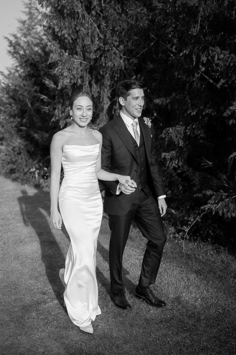 A bride and groom share a candid moment while walking outdoors in black and white photography.