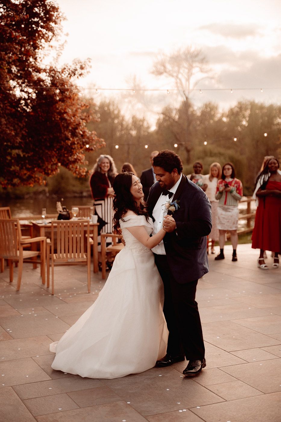 A couple shares their first dance on an outdoor patio during a romantic autumn wedding celebration at sunset.