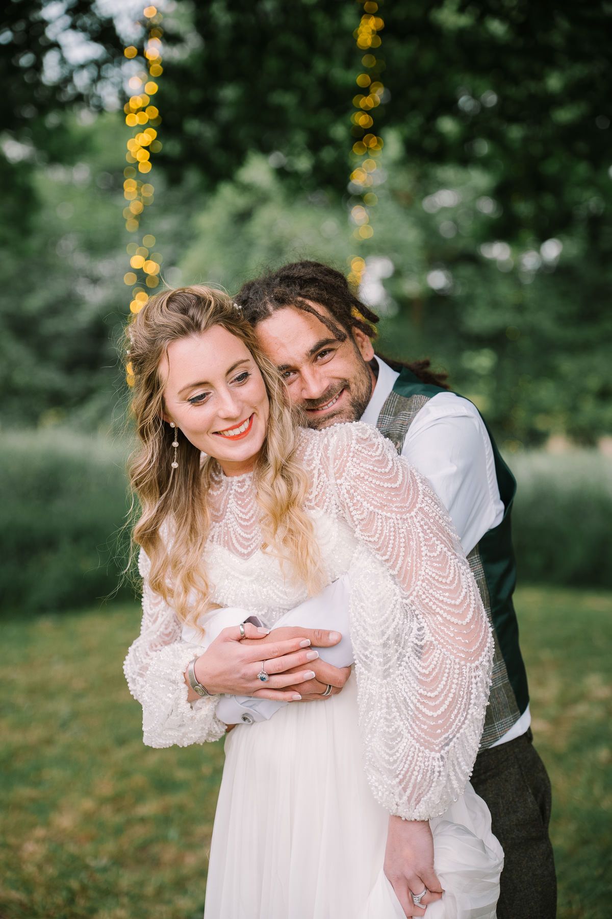 A bride and groom embracing in a garden setting with string lights hanging overhead.