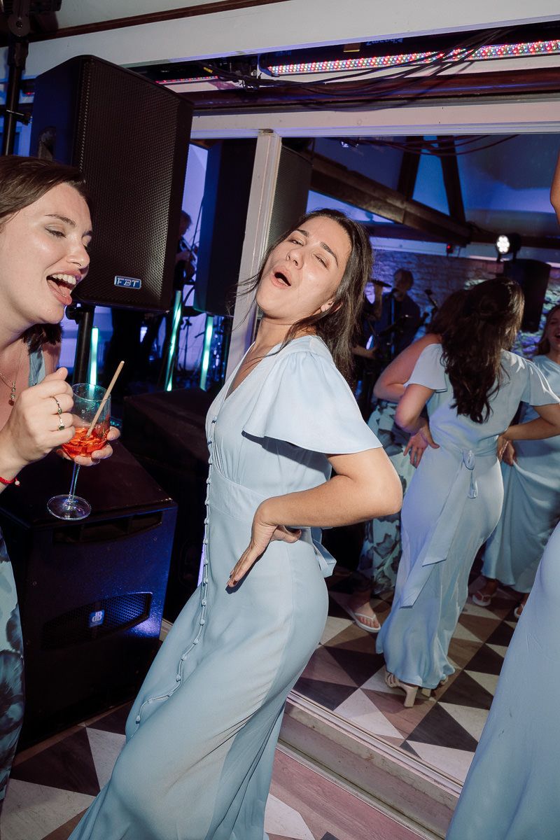 People in matching light blue outfits dancing and laughing at a party with colorful lighting and drinks.