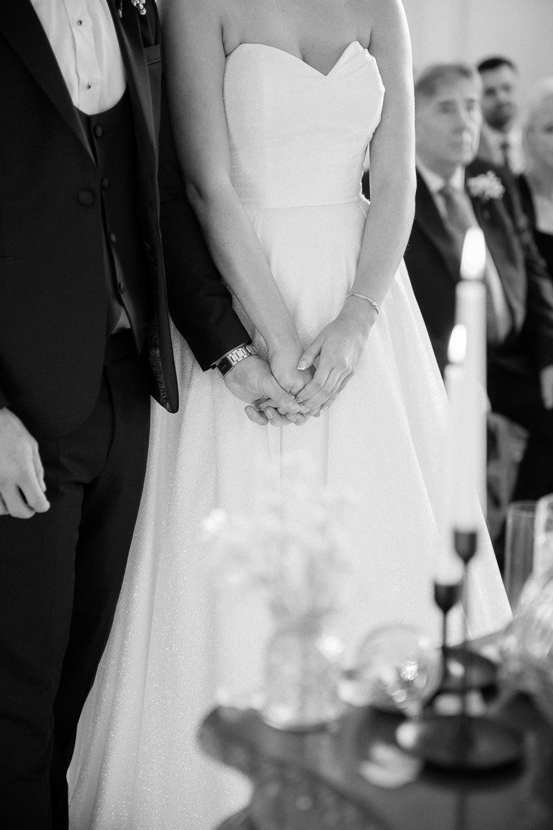 Close-up view of bride and groom's hands during wedding ceremony in black and white.