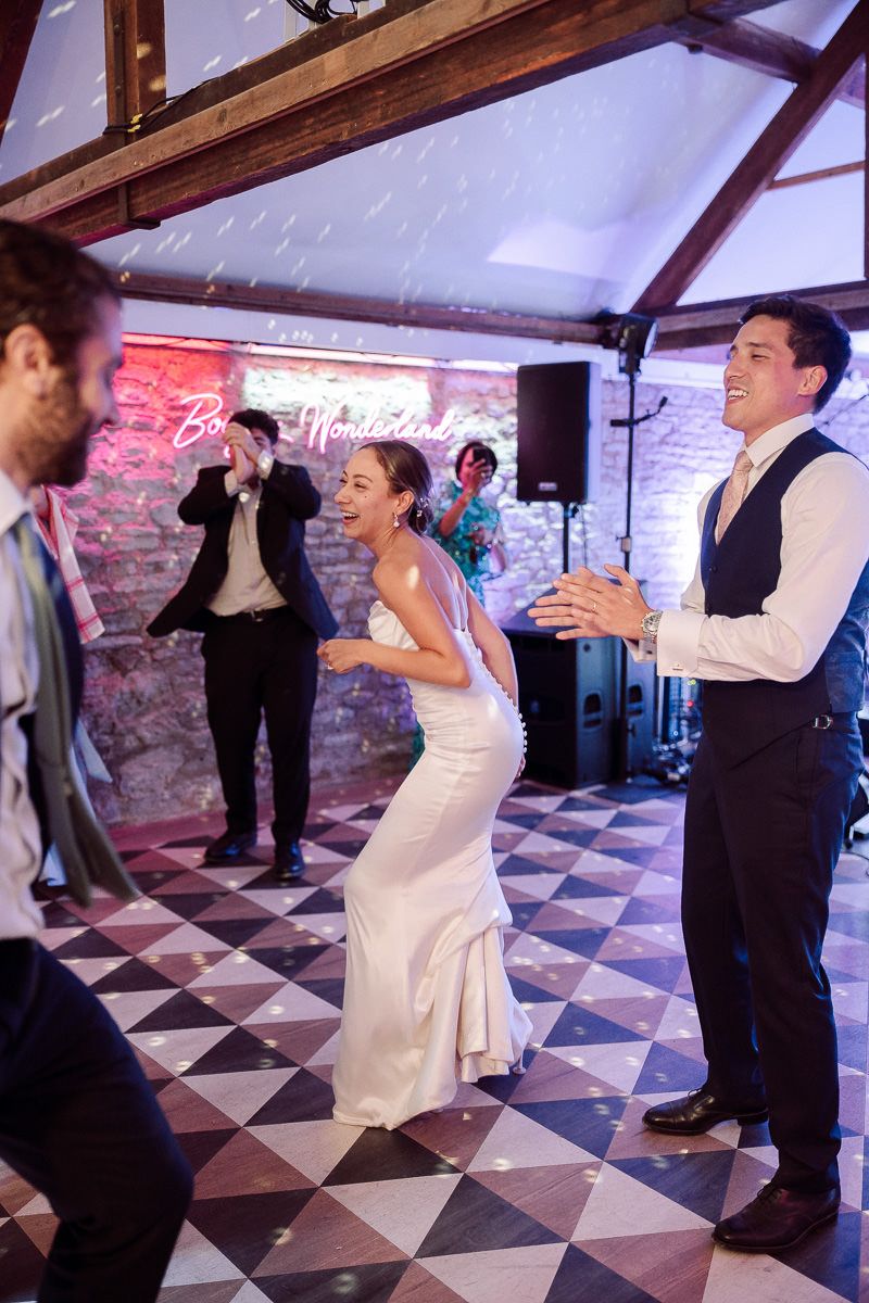 People dancing and celebrating at a wedding reception on a black and white checkered dance floor with brick walls and mood lighting.