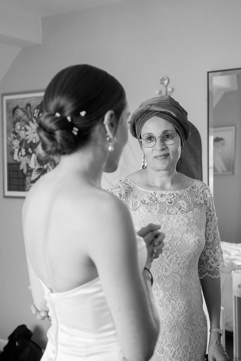 A series of black and white photos showing a bride getting ready with someone in a lace dress helping her.