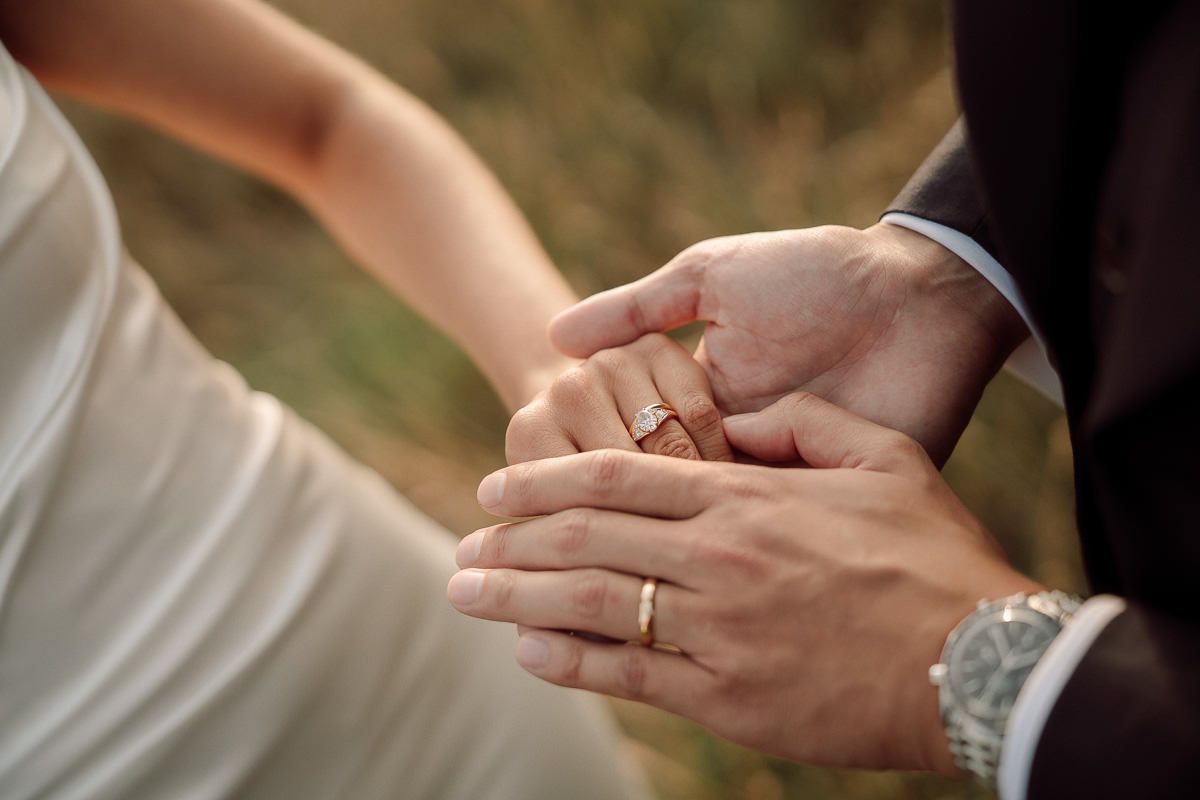 Close-up view of hands exchanging wedding rings during an outdoor ceremony.