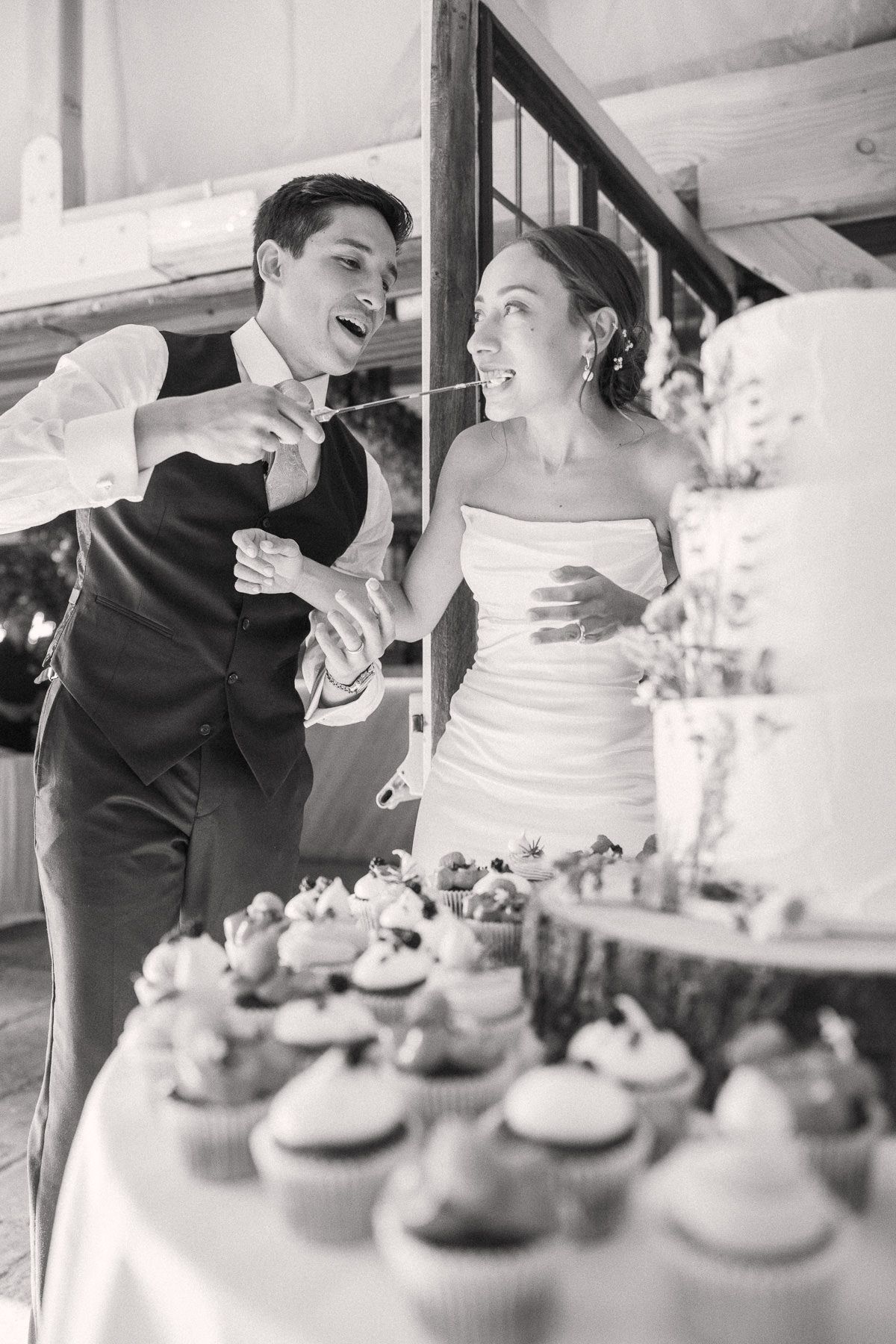 A black and white image of a smiling couple standing next to a table with a wedding cake.