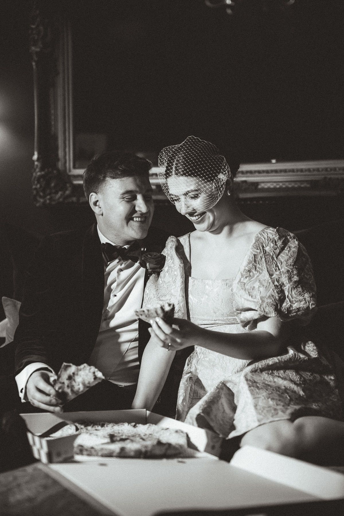 Two people sit side by side in dim lighting sharing a tender moment reading by illuminated light.