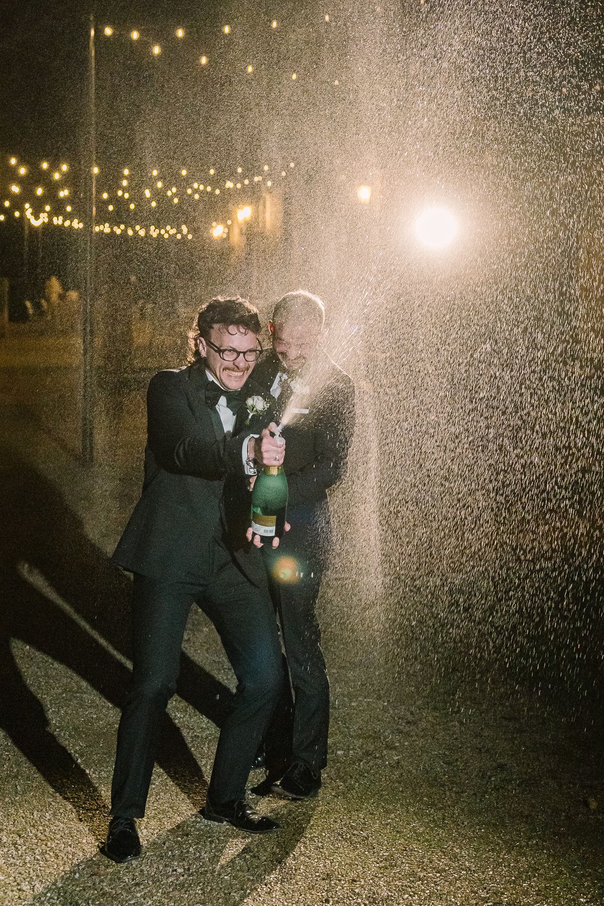 A couple embracing in the rain under string lights at night, creating a romantic and atmospheric scene.