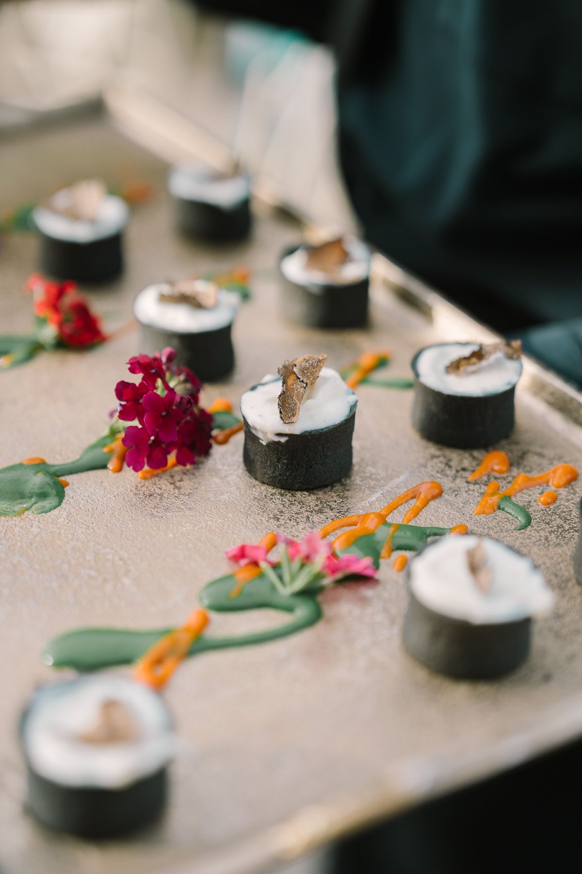 A tray of sushi rolls decorated with fresh red flowers and greenery on a wooden surface.