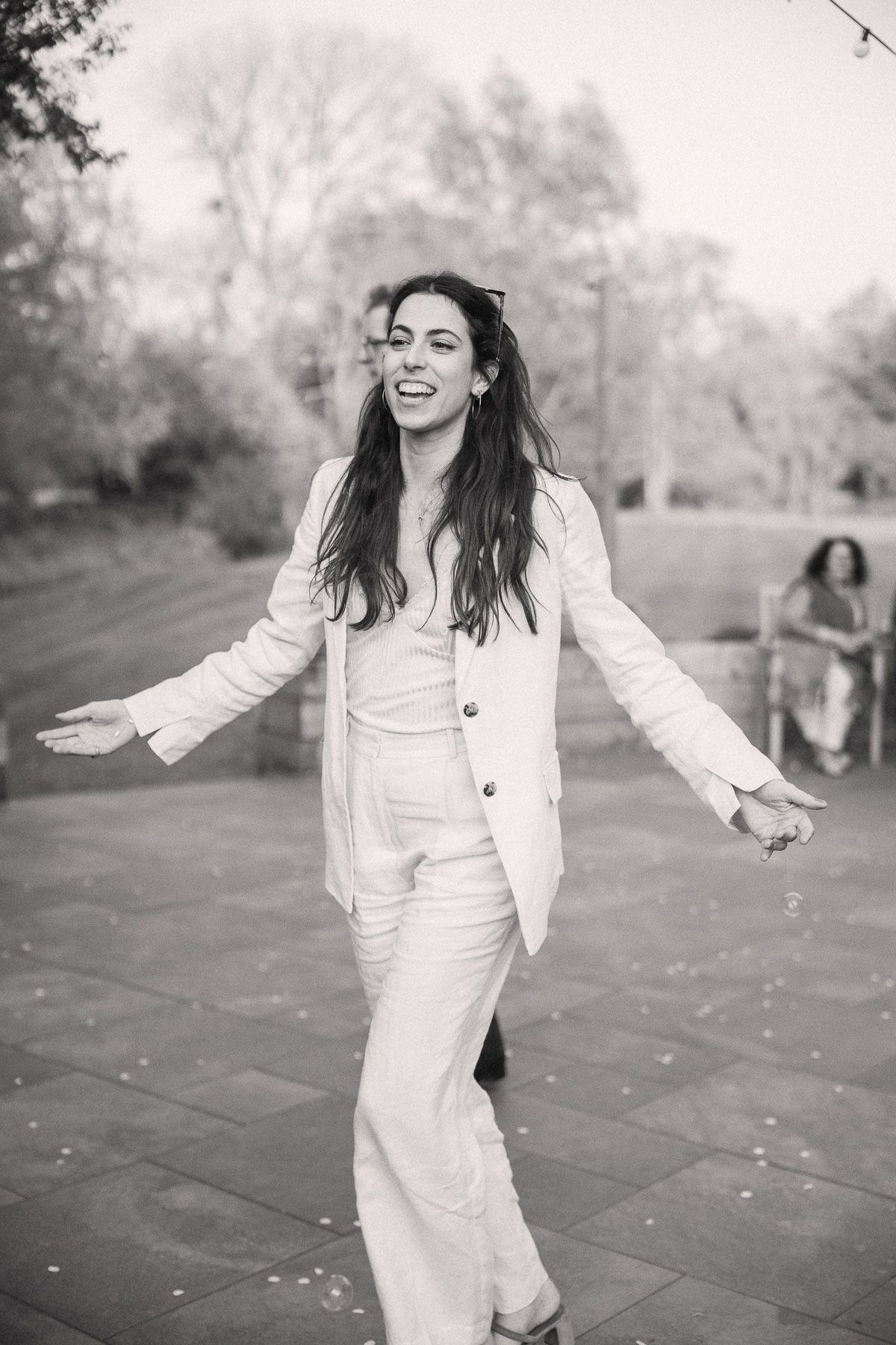 A young woman with long dark hair smiling and walking in an outdoor setting.