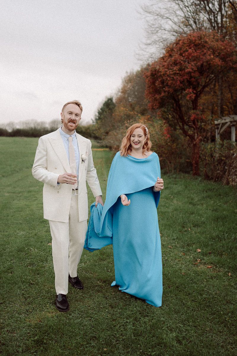 A couple shares a playful moment with a blue blanket in an autumn field with red berry bushes in the background.