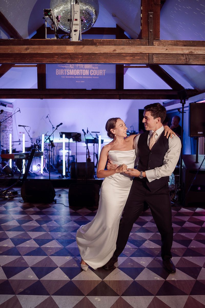 A couple performs an elegant dance dip move on a black and white checkered ballroom floor under dramatic lighting.