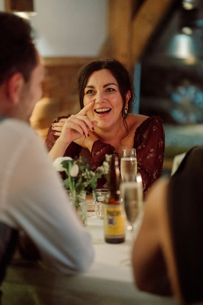 A couple enjoys an intimate dinner conversation at a dimly lit restaurant table with drinks and greenery decor.